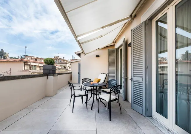 A furnished private terrace with a metal table and chairs under a retractable awning, with rooftops visible beyond the low wall.