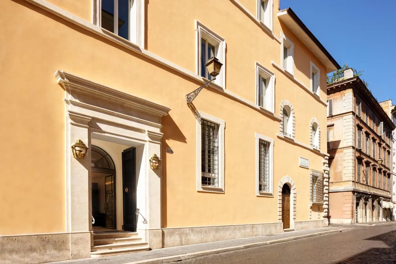 The ochre facade of a building with a stone-framed arched entrance, steps and wall lantern, beside a cobbled street.