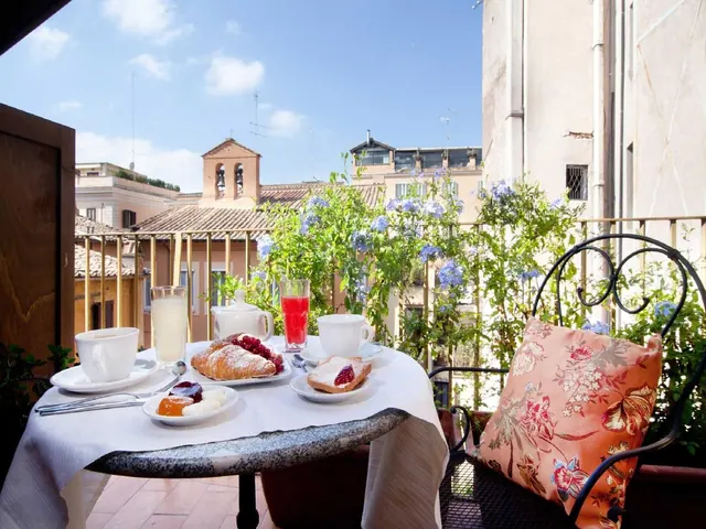 A breakfast table set with pastries, juice and coffee cups sits on a balcony overlooking rooftops and a church bell tower.