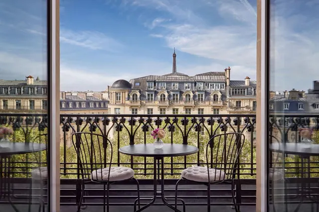 A furnished balcony overlooks Paris rooftops with the Eiffel Tower visible in the distance.