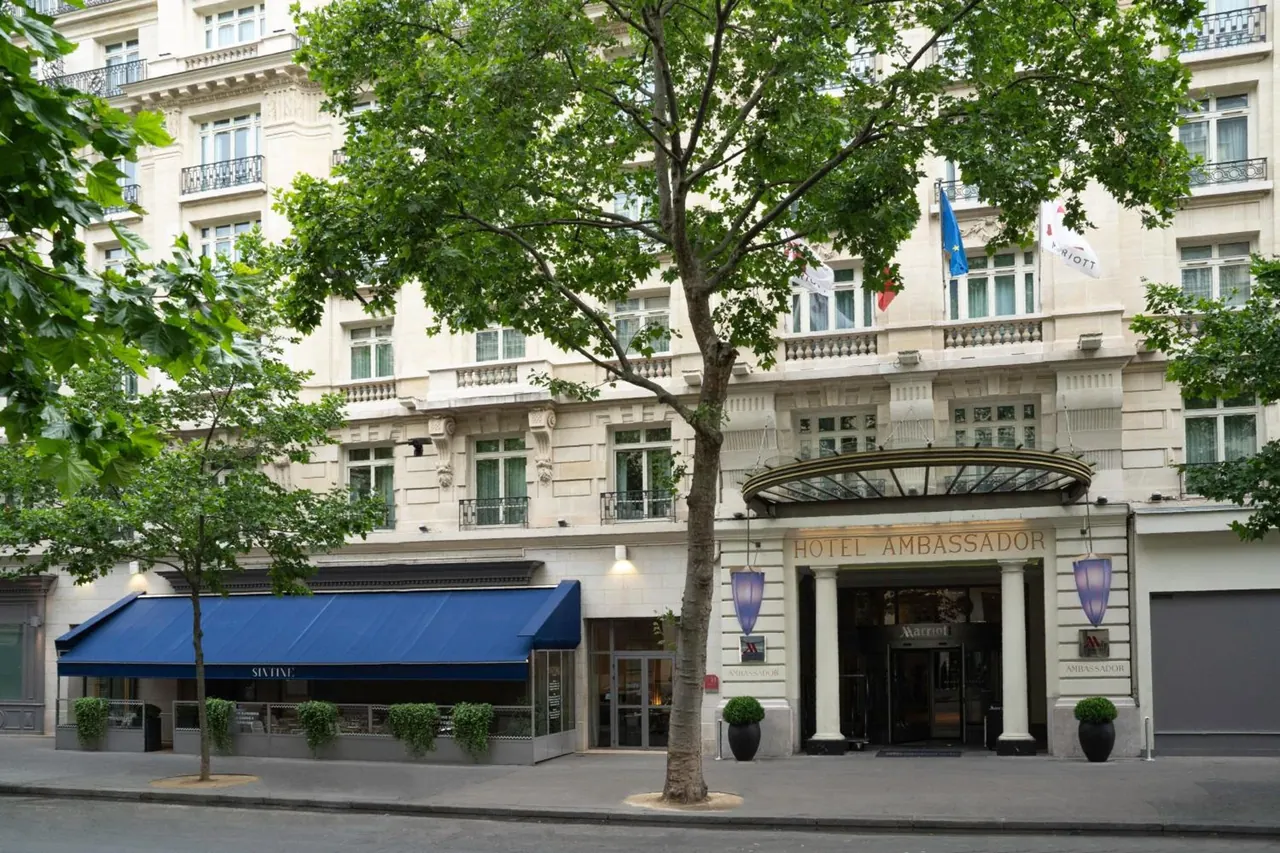 The Hotel Ambassador entrance is shown on a tree-lined Paris street.
