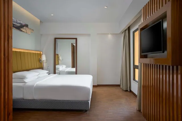 A modern bedroom with a double bed, wall-mounted television, wood flooring and tall curtained windows.