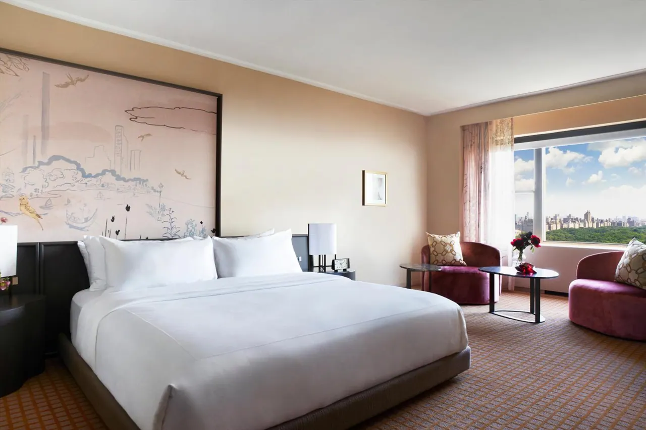 A bedroom with a king bed, a large mural headboard, and a window overlooking a park and city skyline.