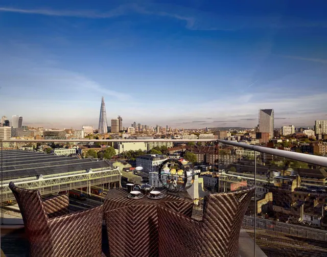 A rooftop terrace with wicker armchairs and a table set with teacups and a cake stand overlooks the London skyline, including The Shard.