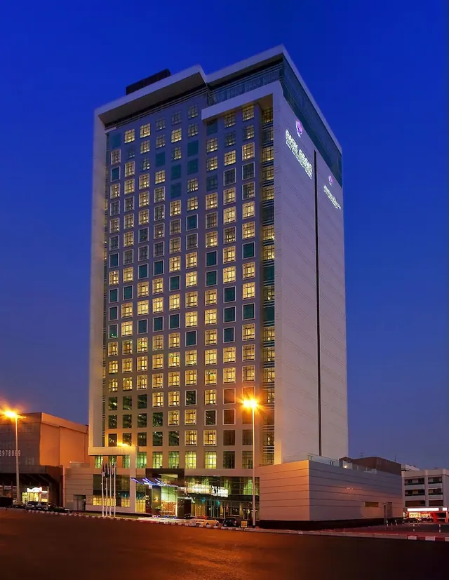 A tall hotel tower with illuminated windows stands under a deep blue dusk sky, with its entrance and street lights visible at the base.