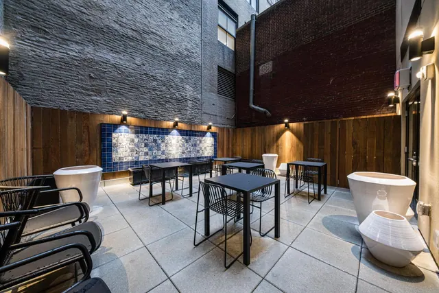 An outdoor courtyard seating area with black metal tables and chairs, white planters, a blue tiled wall and brick walls.