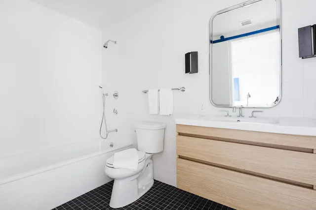 A white bathroom with a bathtub and shower fixture, a toilet, a wood-front vanity with a single basin, and a framed wall mirror.