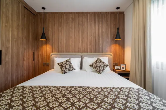 A bedroom with a king bed, wood-panelled walls, two black pendant lights and a patterned throw at the foot of the bed.