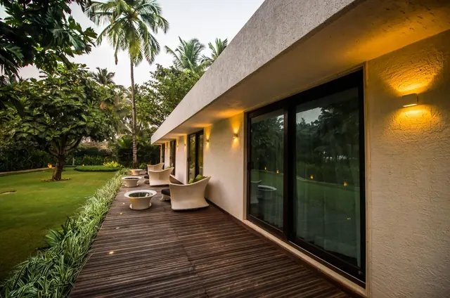 A low modern building opens onto a wooden deck with lounge chairs beside a landscaped tropical garden.