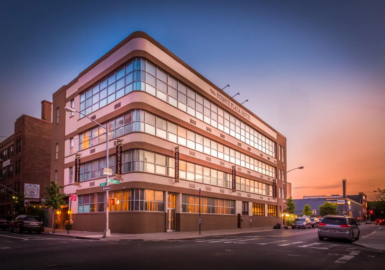 Exterior of the Pointe Plaza Hotel building at dusk, with lit windows, vertical banners on the facade and parked cars on the street.