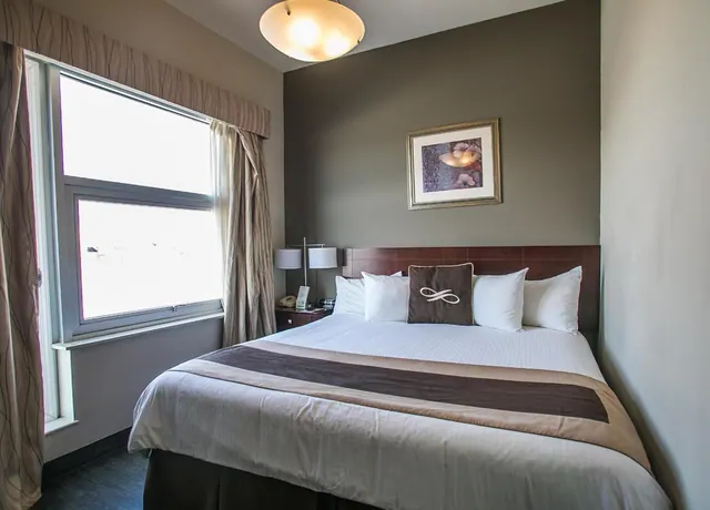 A bedroom with a made double bed, bedside lamps, a framed picture on the wall and a window with curtains.