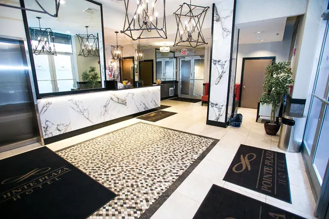 A hotel lobby with a marble front desk, black metal chandeliers, a patterned tile rug, and branded doormats near the entrance.