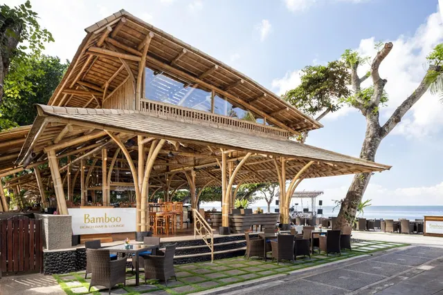 Exterior of the Bamboo Beach Bar & Lounge, an open-sided bamboo building with outdoor tables and chairs, with the sea visible behind it.
