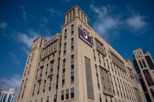 A low-angle view of a beige hotel tower with a purple Premier Inn sign under a blue sky.