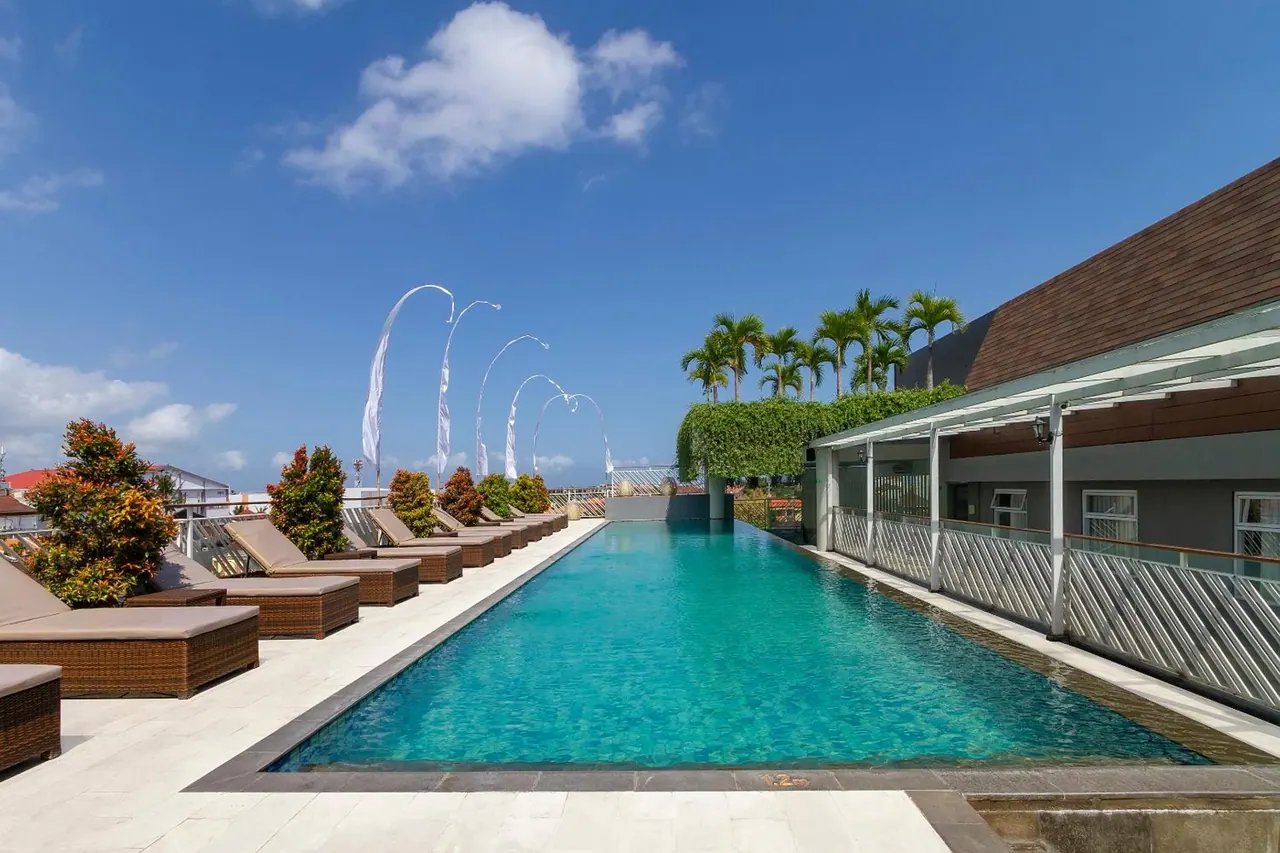 A long lap pool lined with brown wicker sun loungers and white decorative flags under a blue sky.
