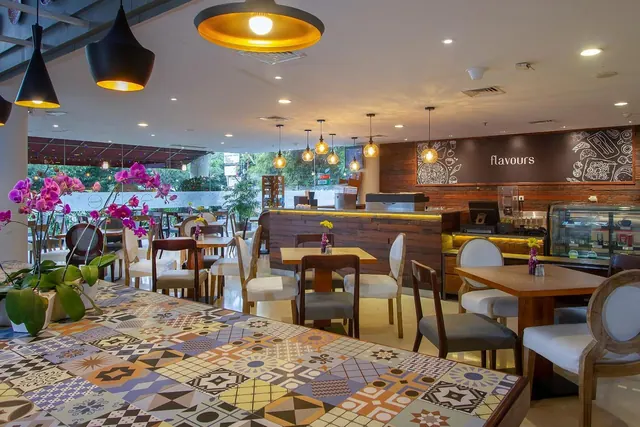 A restaurant dining room with patterned tile floors, pendant lights, pink orchids on a table, and a bar counter with a sign reading flavours.