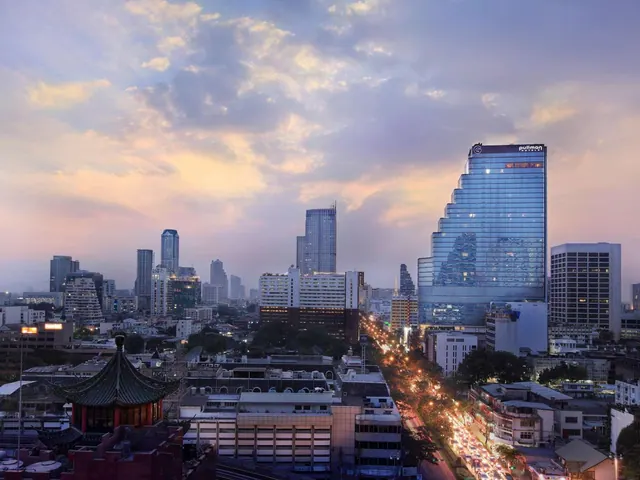 Dusk view over a Bangkok skyline showing a tall glass hotel tower with a Pullman sign, a red pavilion roof in the foreground and a lit road with traffic below.