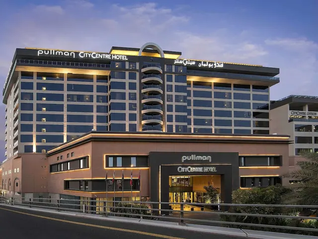 Exterior of the Pullman City Centre Hotel at dusk, showing its illuminated tower, entrance canopy and signage.