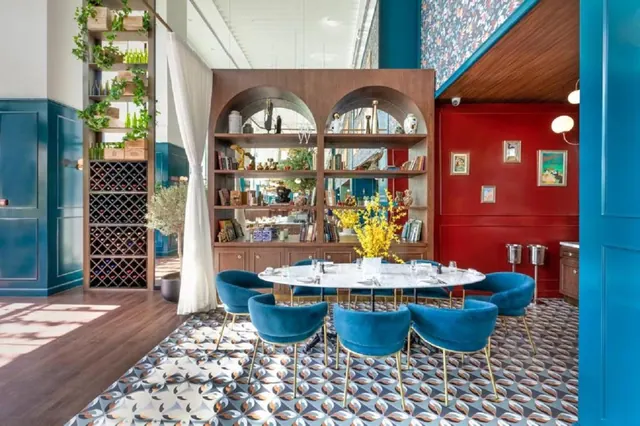 A dining room with blue upholstered chairs around a round marble table, a patterned tile floor, arched wooden shelves and a wine rack.