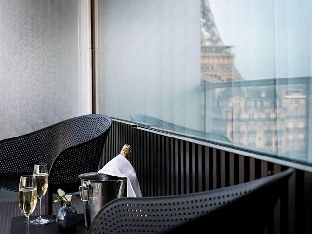 A terrace seating area with champagne glasses and a view of the Eiffel Tower through the windows.
