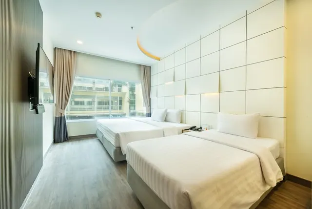 A hotel bedroom with two single beds with white bedding, a wall-mounted television, and a window looking onto a neighbouring building.