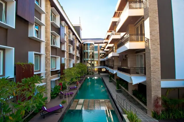 A long lap pool runs between two multi-storey hotel buildings, with purple sun loungers along the left edge and balconies on the right.