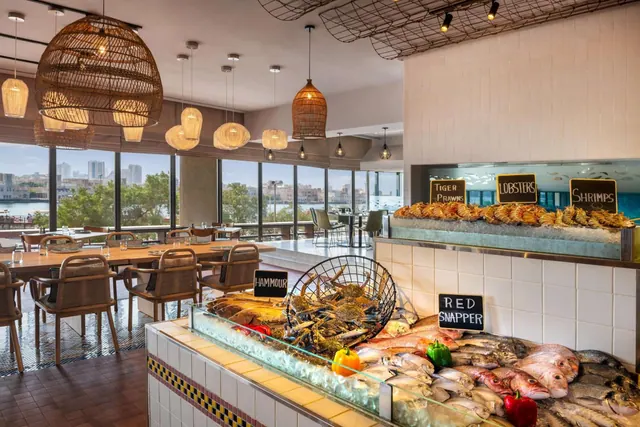 A restaurant dining room with a seafood display on ice in the foreground and floor-to-ceiling windows overlooking the water and city buildings.