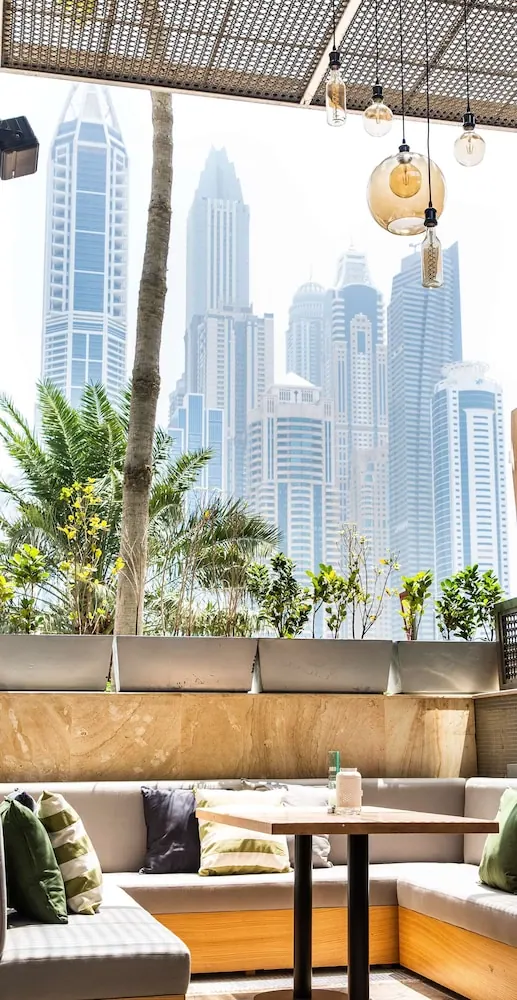 An outdoor lounge with cushioned banquette seating and a wooden table, with high-rise towers and palm trees visible beyond the terrace edge.
