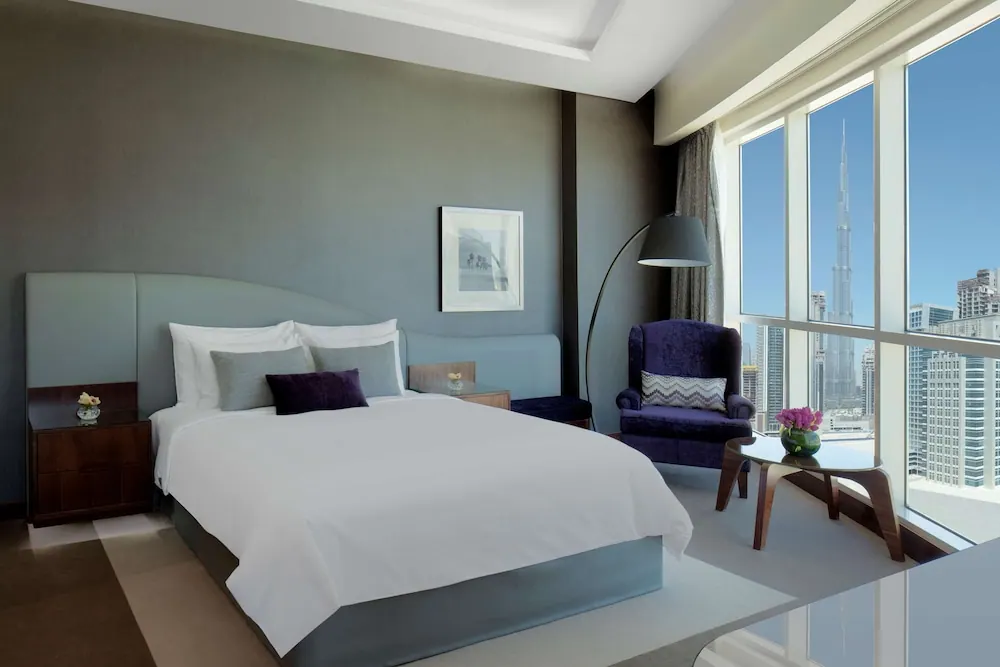 A bedroom with a king bed, a purple armchair and floor-to-ceiling windows showing the Burj Khalifa and surrounding city towers.