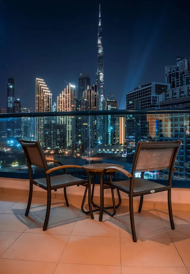 A night view from a balcony with two chairs and a small round table, looking out over the Dubai skyline with the Burj Khalifa in the centre.