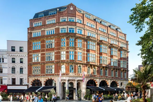 Exterior of a multi-storey red brick hotel building with the Hampshire name above the entrance, with pedestrians on the street below.