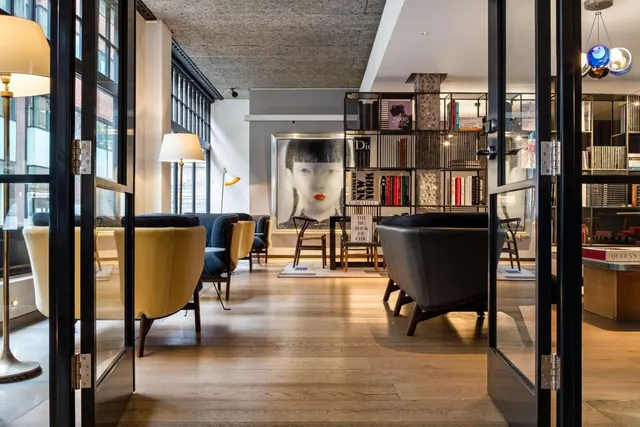 A lounge with yellow and dark armchairs, glass doors in the foreground, bookshelves and a framed portrait on the back wall.