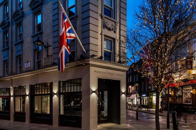 The exterior of Mercer Street Hotel at dusk, with a Union Jack flag on the corner facade and a tree strung with lights on the street.