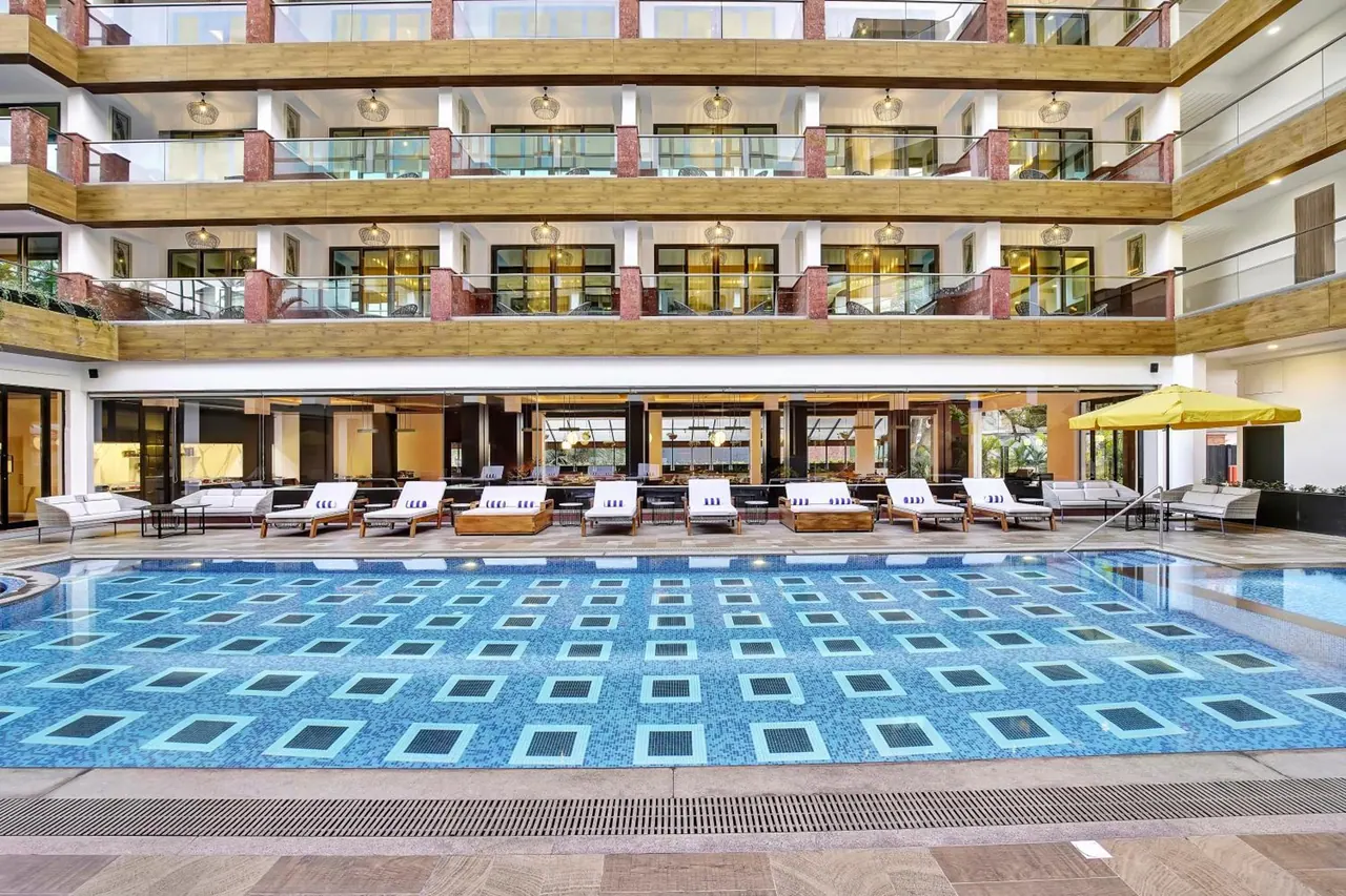 A large patterned pool is surrounded by sun loungers and umbrellas in the hotel courtyard.