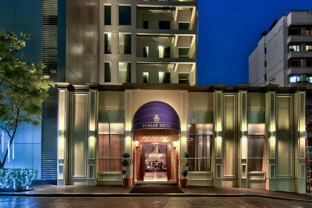 Dusk view of the Punjab Grill restaurant entrance with a purple arched canopy, illuminated pilasters and a lit doorway.