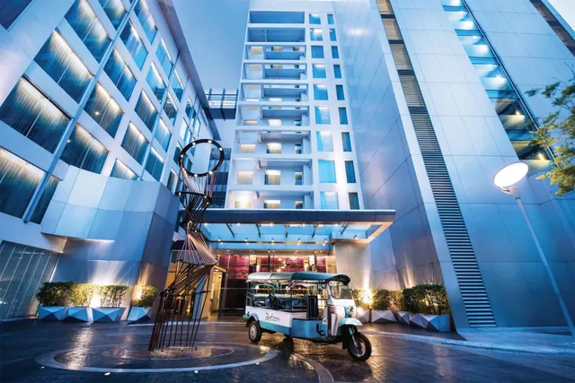 The hotel's tower and covered entrance at dusk, with a parked tuk-tuk, a metal sculpture and planters in the forecourt.
