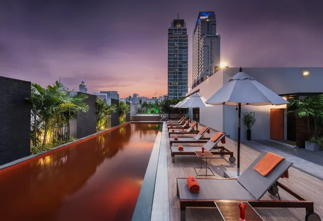 A rooftop pool at dusk with sun loungers, parasols and high-rise towers in the background.
