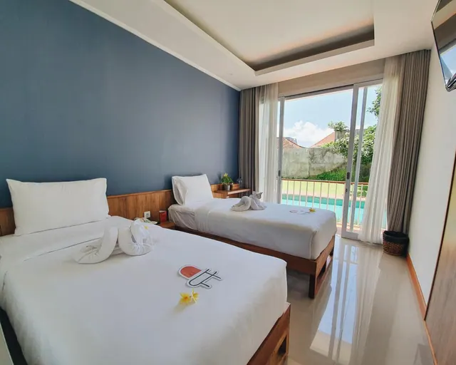 A bedroom with two single beds, a blue accent wall, and a sliding glass door looking out onto a swimming pool and greenery.