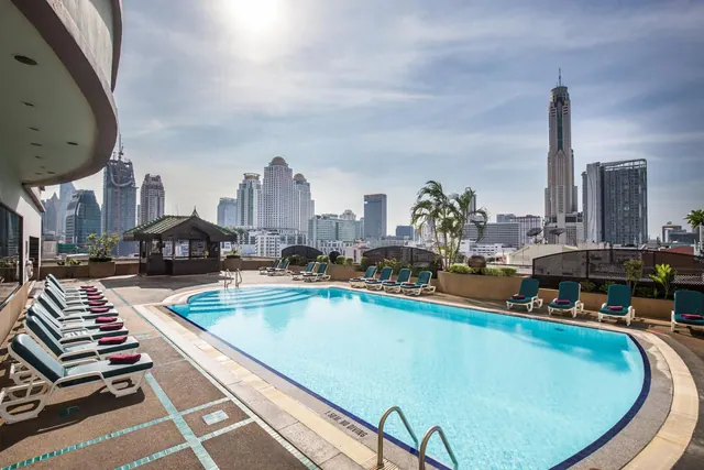 A rooftop swimming pool with teal-cushioned sun loungers along its edge, with high-rise towers visible in the city behind.