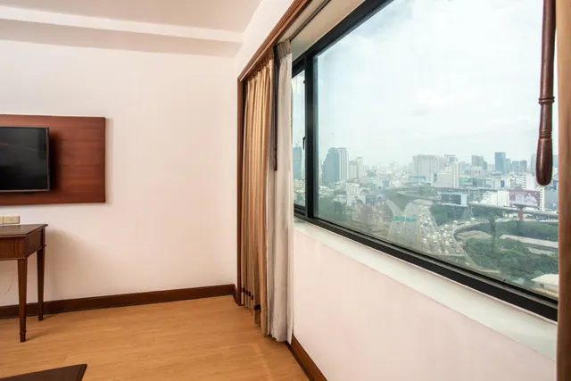 A room corner with a wall-mounted television, a wooden side table, and a large window looking over a city skyline and a busy elevated highway.