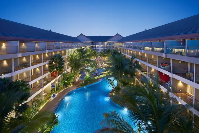 Elevated twilight view of a winding hotel pool surrounded by palm trees and multi-storey guest room balconies.