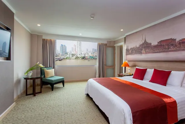 A bedroom with a king bed, red cushions, a temple mural on the headboard wall, an armchair, and a window looking out over a river and city buildings.