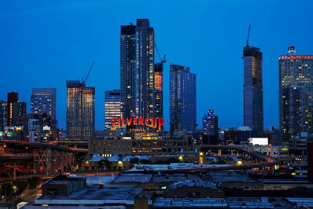 Dusk view over a city skyline with illuminated high-rise towers and the lit Silvercup Studios sign.