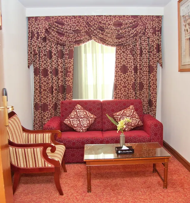 A red upholstered sofa, a striped armchair and a glass-topped coffee table sit in front of a window with patterned curtains.