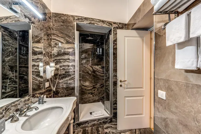 A bathroom with brown marble walls, a pedestal sink, a glass-enclosed walk-in shower and white towels on a wall rail.