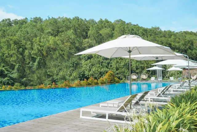 A swimming pool with white sun loungers and umbrellas on a timber deck, with forested hills behind.