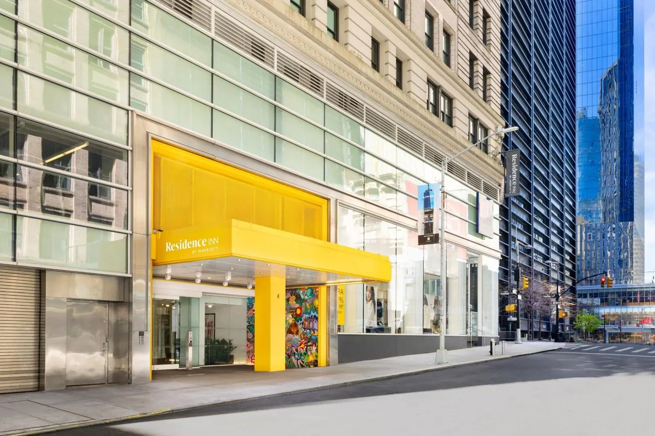 The photo shows the yellow entrance canopy and glass facade of a Residence Inn by Marriott building on a city street.