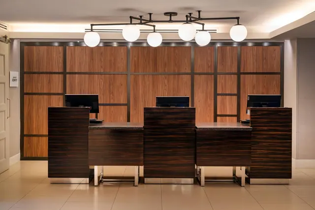 The reception area has four dark wood-veneer front desks with computer monitors, a wood-panelled wall behind them, and globe pendant lights overhead.