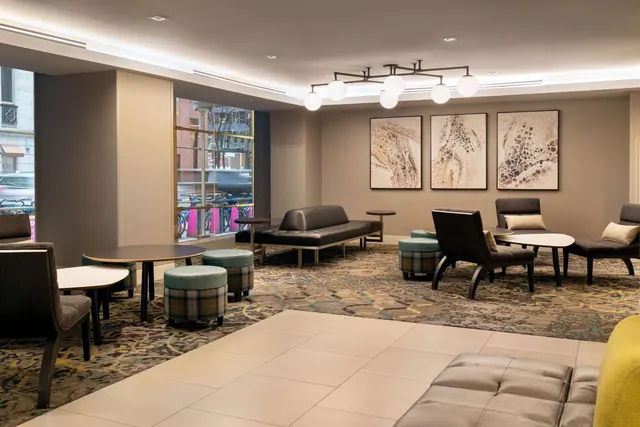 A lounge seating area with armchairs, ottomans, a leather sofa and framed abstract artwork, with a window onto a street.