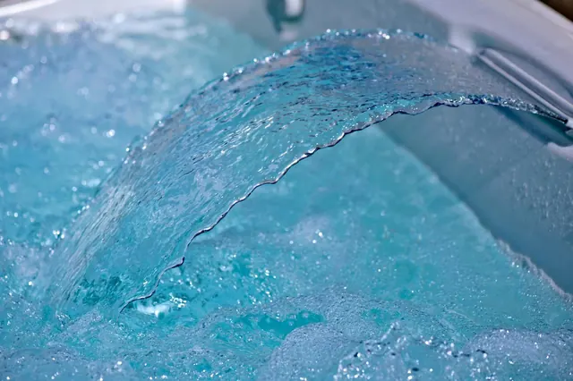 Close-up of water flowing over a spout into a hot tub filled with bubbling blue water.